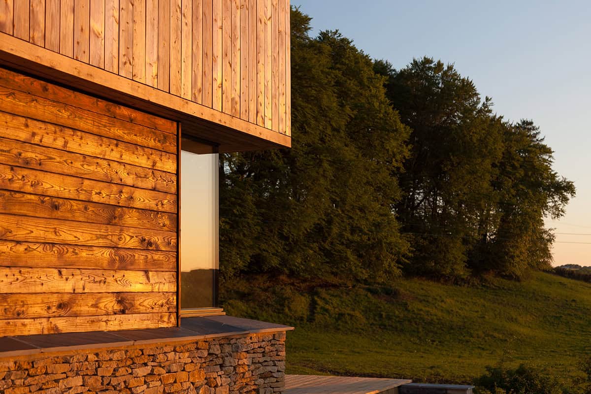 The Larch House larch cladding detail at golden hour with Cotswold stone base and rural hillside